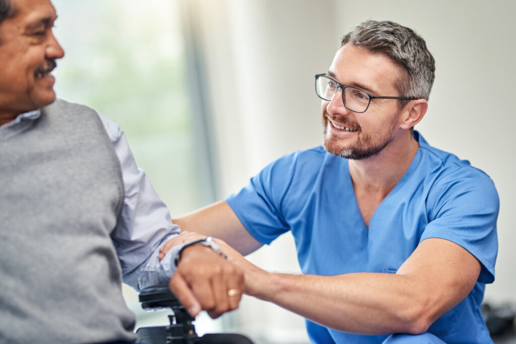 A happy male nurse sits at eye level with memory care resident and engage in conversation. Traditions of Aboite in Fort Wayne, IN.
