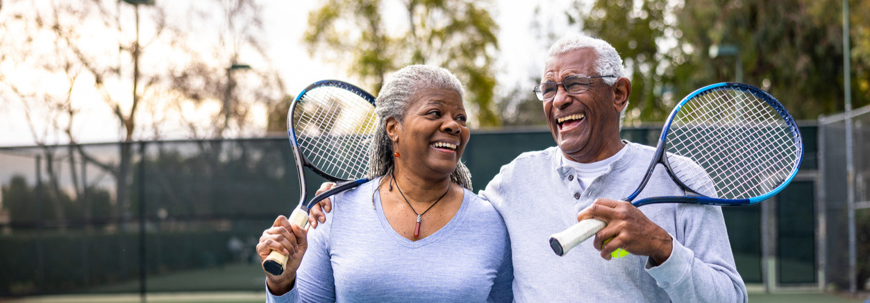 Elderly African American Couple Holding Tennis Rackets smiling together.